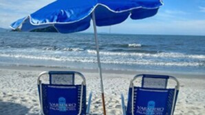 Dos sillas de playa azules con una sombrilla azul sobre arena.