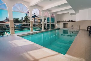 Una piscina interna con pareti di vetro trasparenti, pavimento piastrellato e una scala che conduce a un piano superiore.