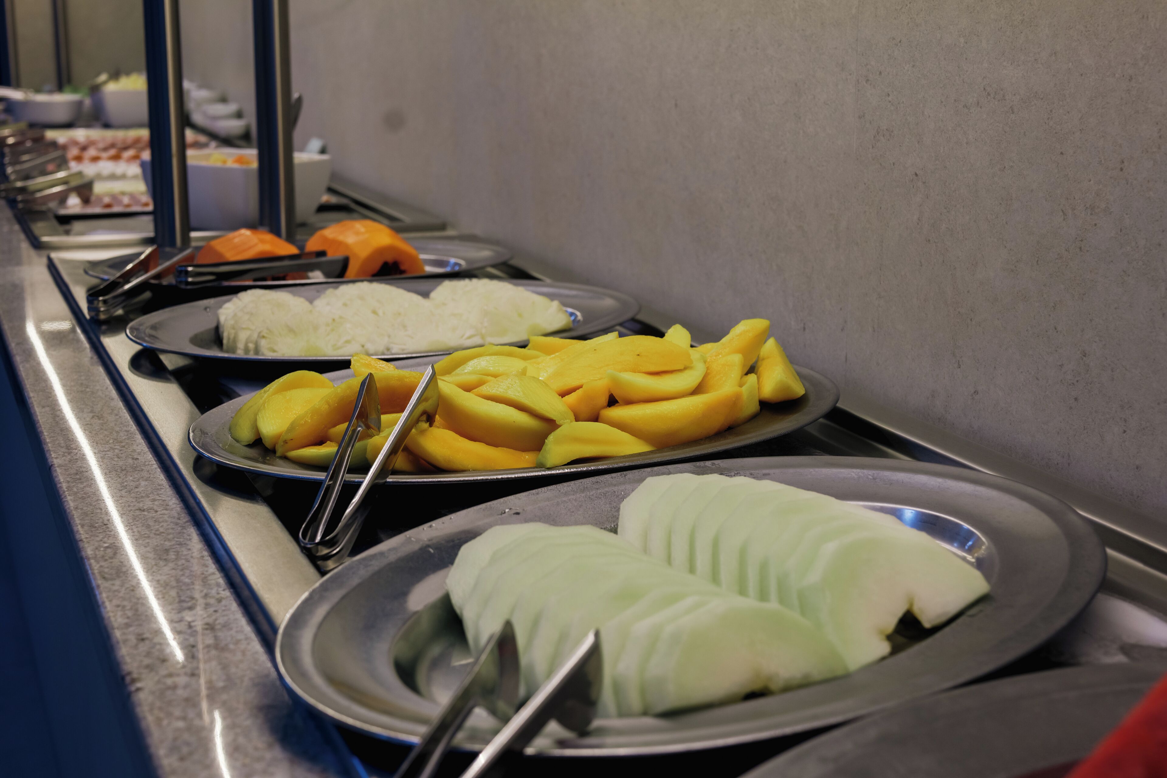 A buffet with various food items including sliced fruits and rice.