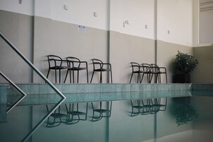 Um espaço moderno e interno com uma piscina de vidro que reflete cadeiras e um letreiro fixado na parede.
