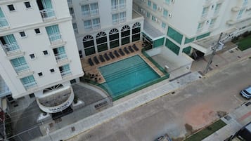Un hotel de varios pisos con piscina en la azotea, zona de estar al aire libre y una fuente circular.