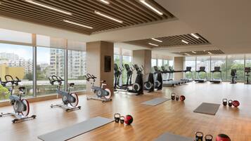 Un gimnasio espacioso con diversos equipos de ejercicio, ventanas amplias y vistas a la ciudad.