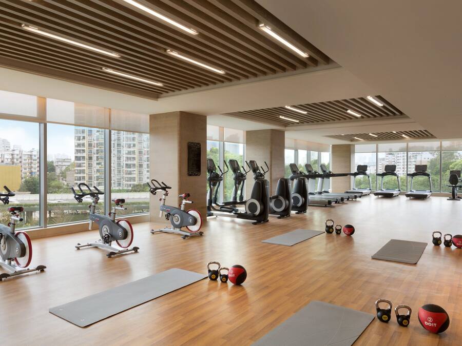 Un gimnasio espacioso con diversos equipos de ejercicio, ventanas amplias y vistas a la ciudad.