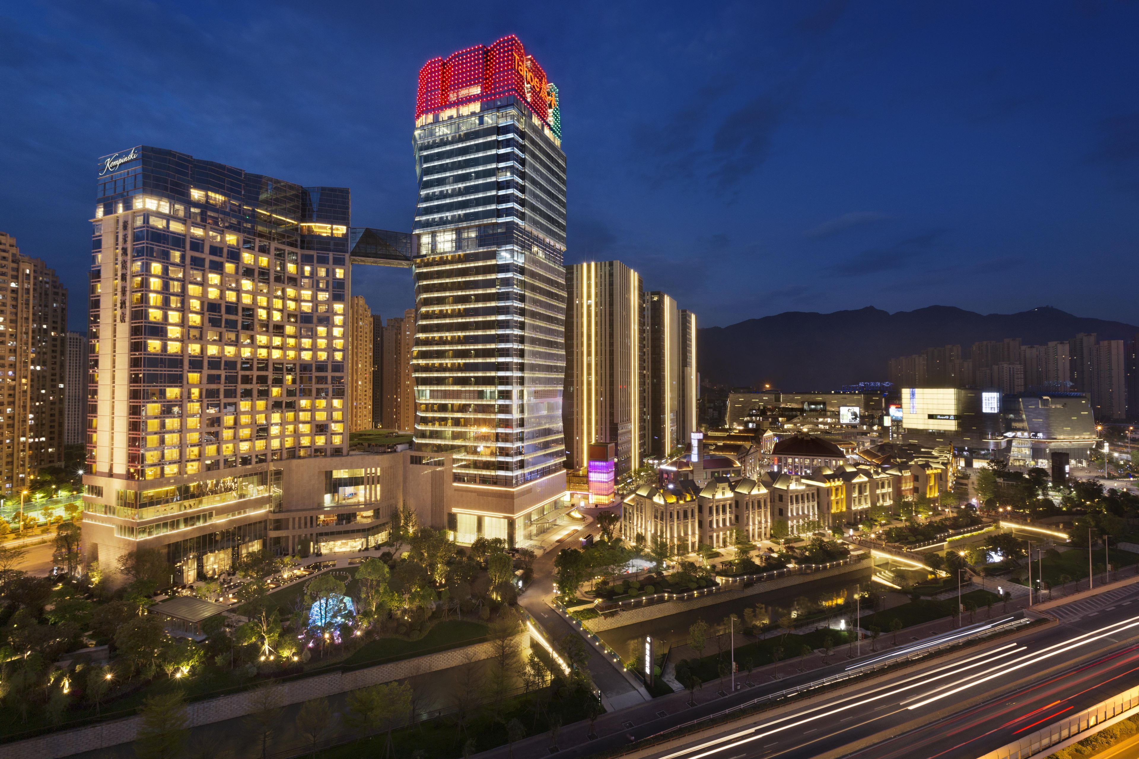 A high-rise hotel with multiple floors, a prominent red sign on top, and a well-lit surrounding area.