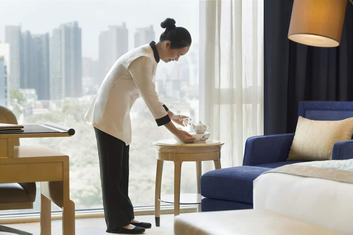 Une chambre d’hôtel avec vue sur la ville, un canapé bleu, une petite table ronde avec une théière et un bureau en bois.