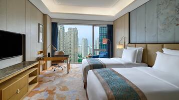 A hotel room with a large bed, a desk, a TV, and a view of tall buildings.
