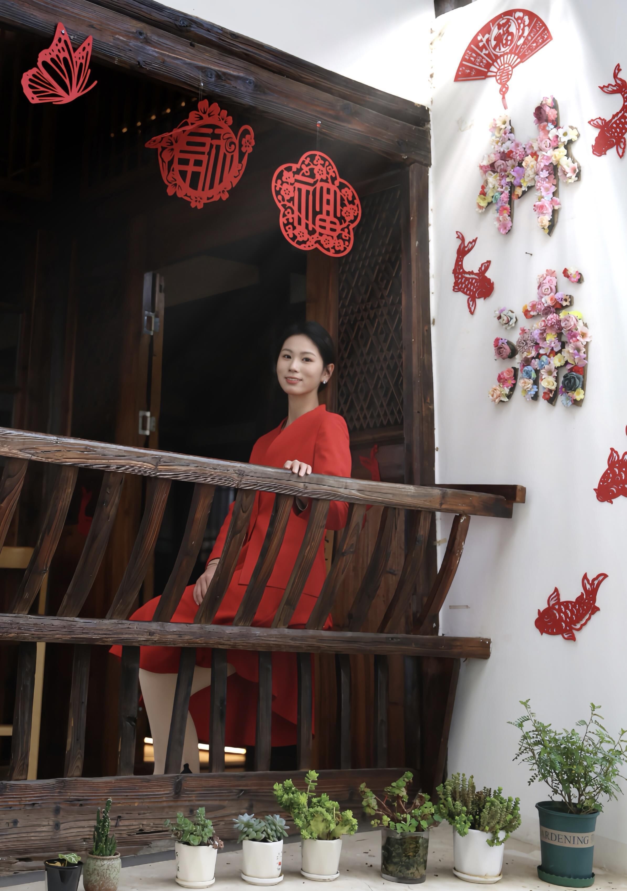 A person in a red dress on a wooden balcony with potted plants below.