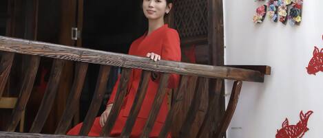 A person in a red dress on a wooden balcony with potted plants below.