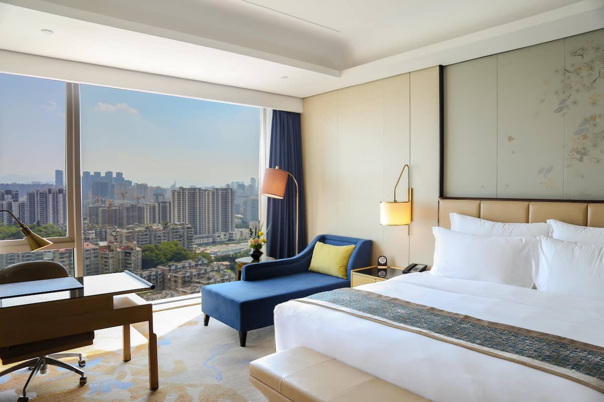 Une chambre d’hôtel avec une grande fenêtre, un lit, un bureau et une chaise.