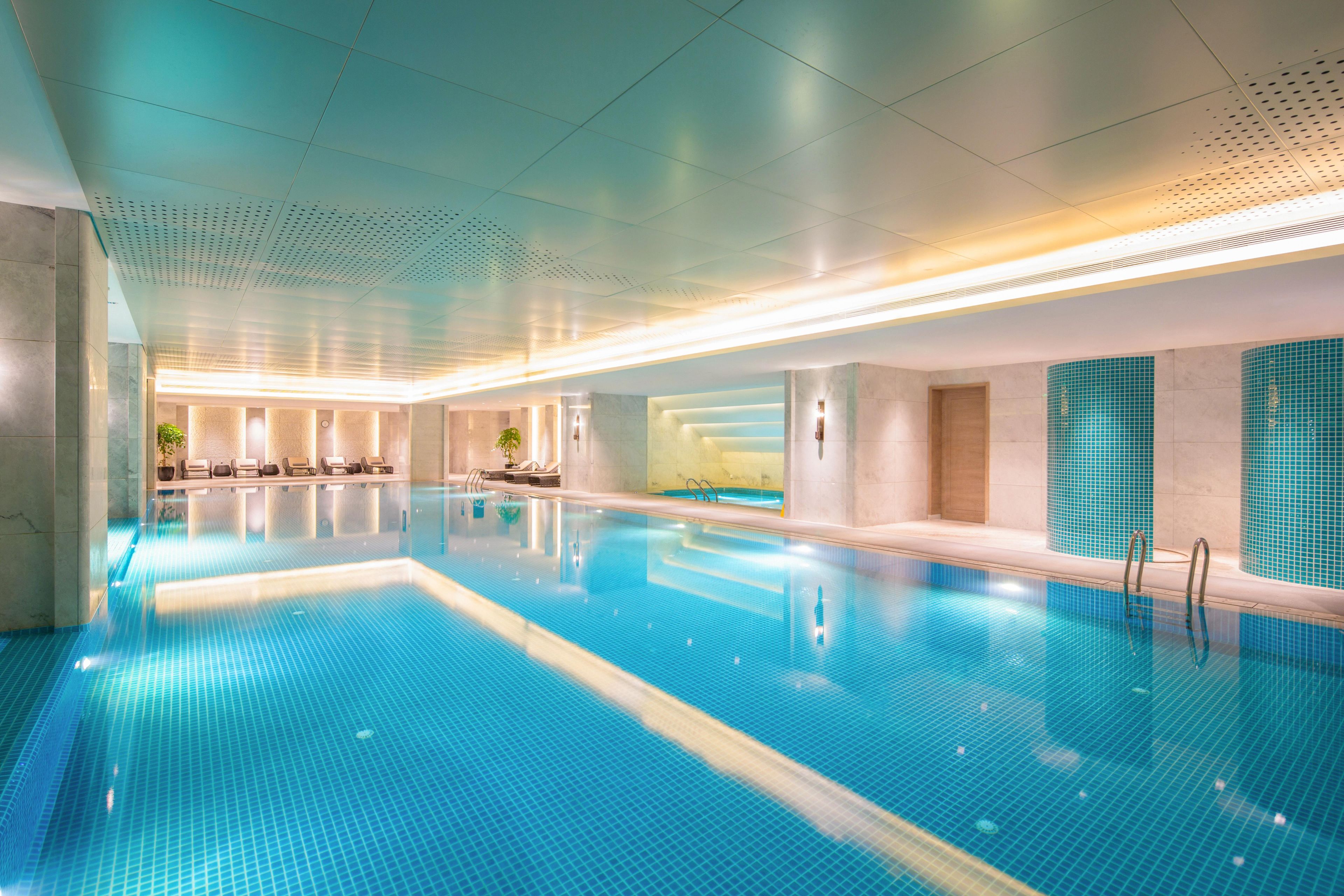 Une grande piscine intérieure à l’eau claire, avec des murs carrelés et un design moderne au niveau du plafond.