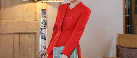 A person in a red outfit standing next to a lamp and a book.