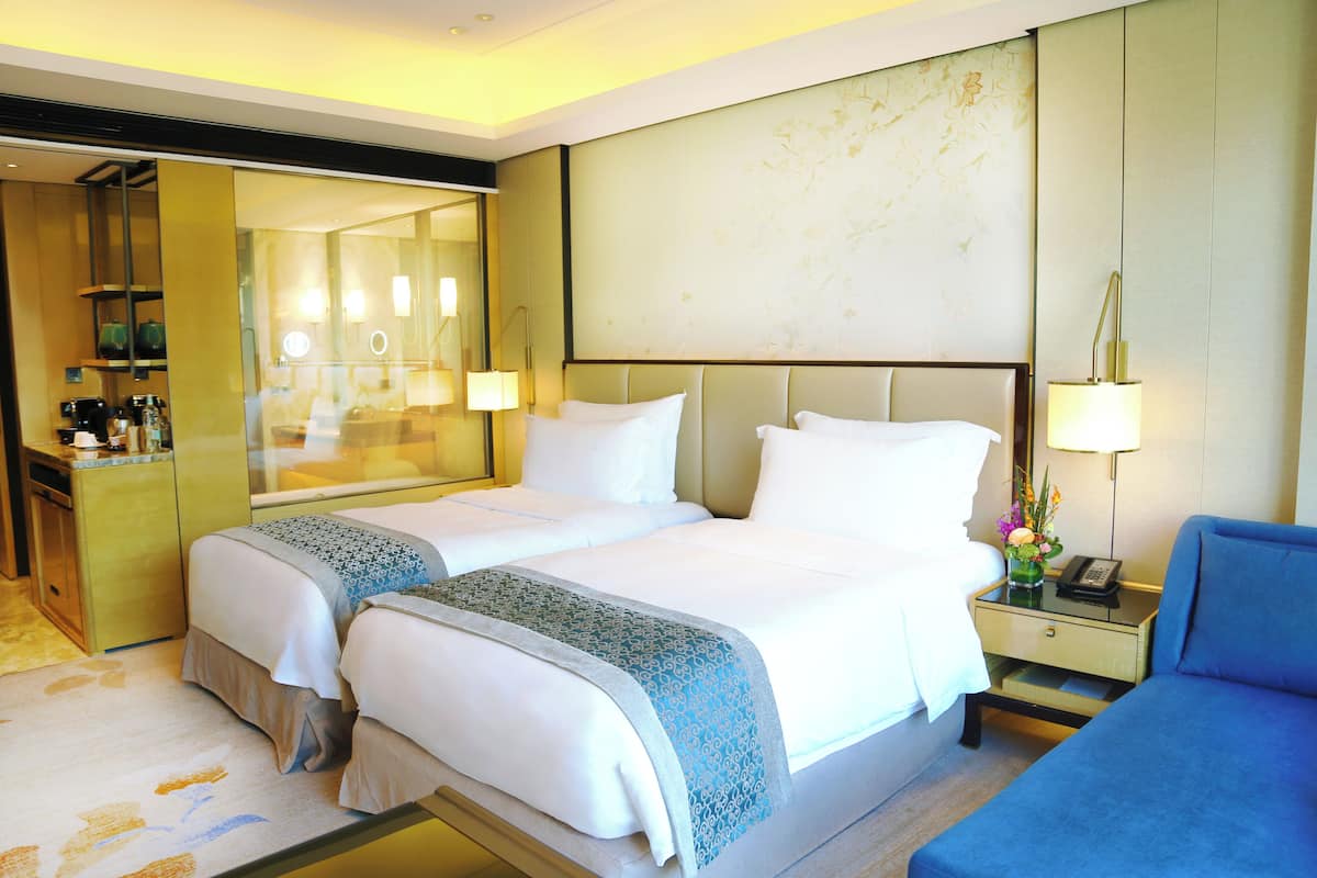 Une chambre d’hôtel avec deux lits, un bureau, une chaise, un miroir et une table de chevet avec une lampe.