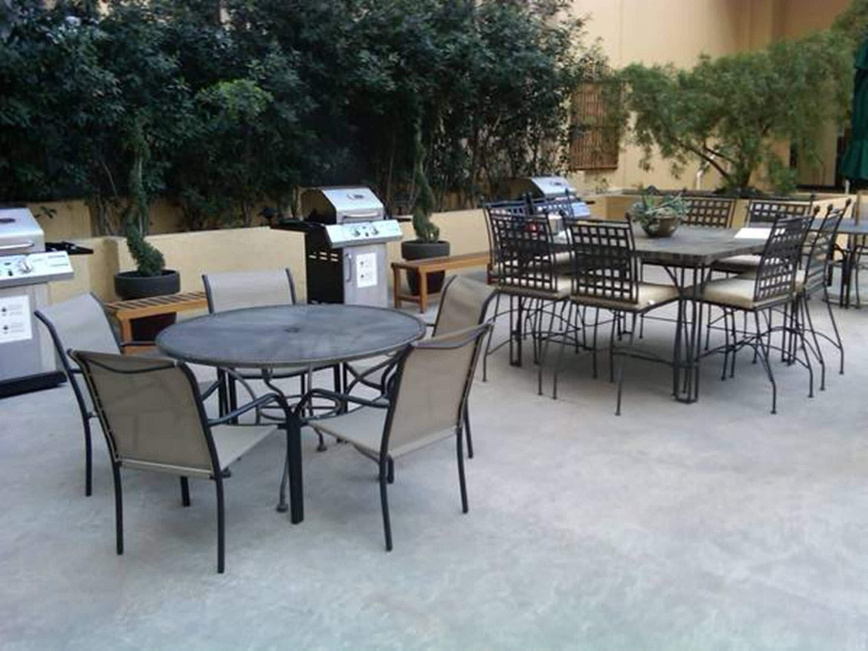Eine Terrasse im Freien mit runden Tischen und Stühlen, einem Grill und Kübelpflanzen.