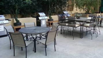 Eine Terrasse im Freien mit runden Tischen und Stühlen, einem Grill und Kübelpflanzen.