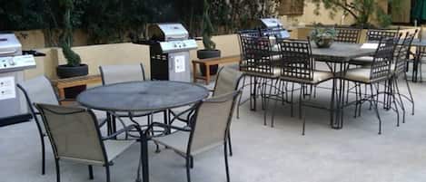 An outdoor patio with round tables and chairs, a grill, and potted plants.