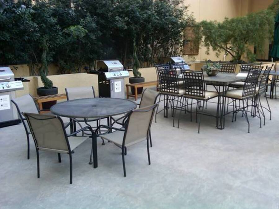 Eine Terrasse im Freien mit runden Tischen und Stühlen, einem Grill und Kübelpflanzen.