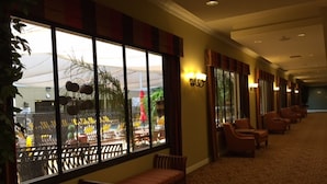 A hotel corridor with a bench, chairs, and a large window overlooking an outdoor area with umbrellas and plants. - GetAways at Jockey Club (Las Vegas)
