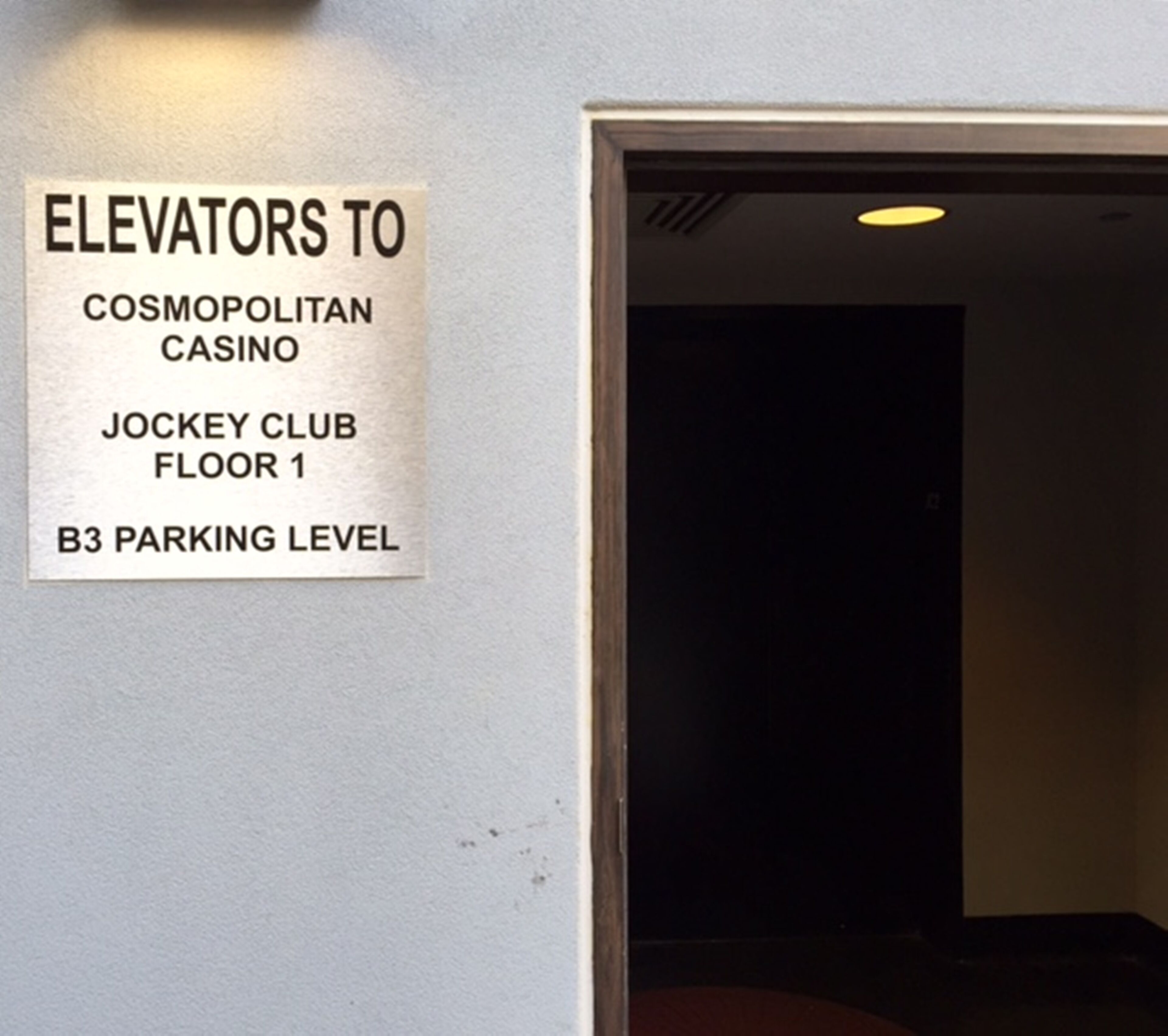 Placa na parede indicando elevadores para o Cassino Cosmopolitan, Jockey Club, andar 1 e nível de estacionamento B3.