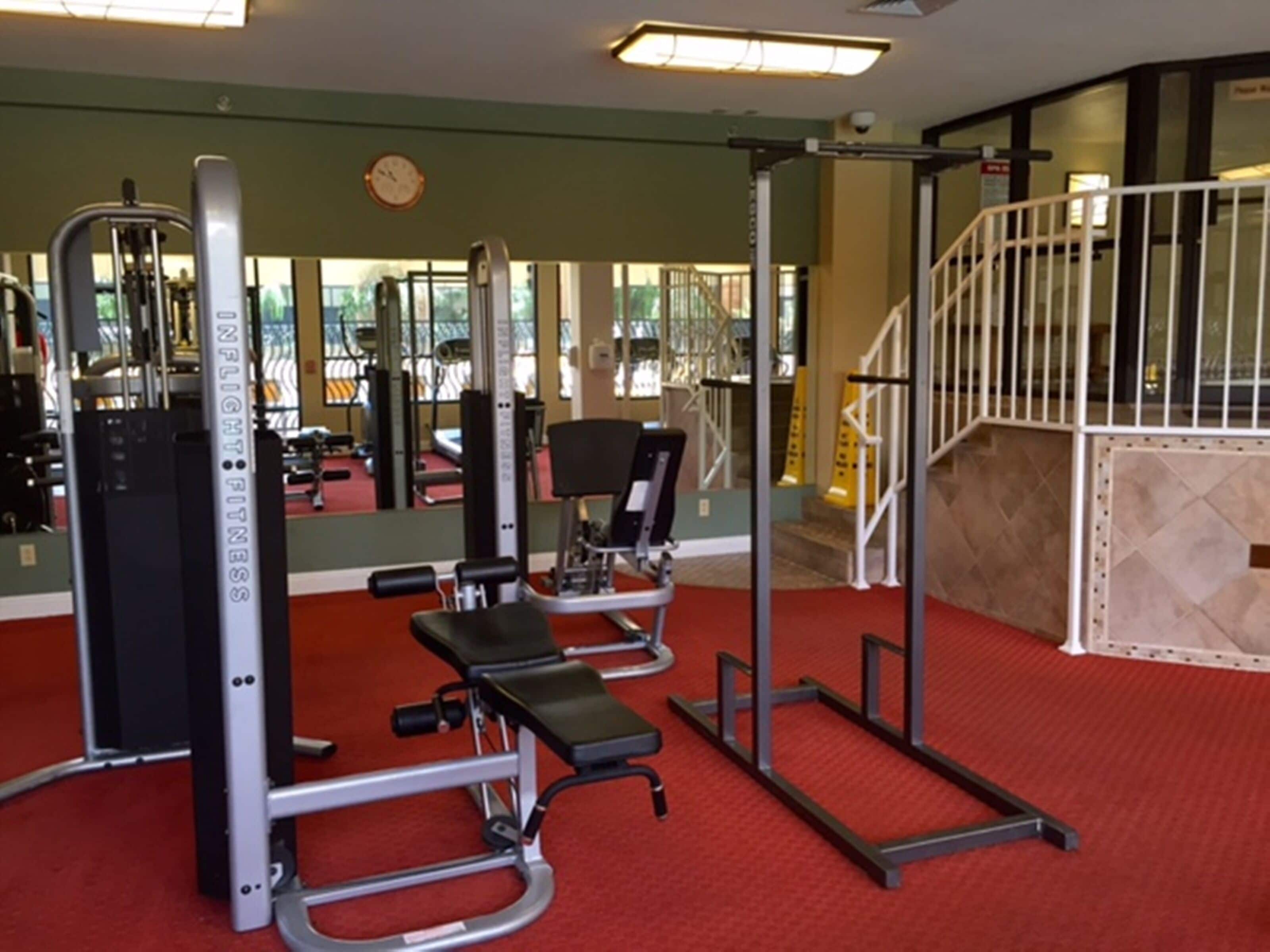 A gym with exercise equipment, a red carpet, and a staircase.