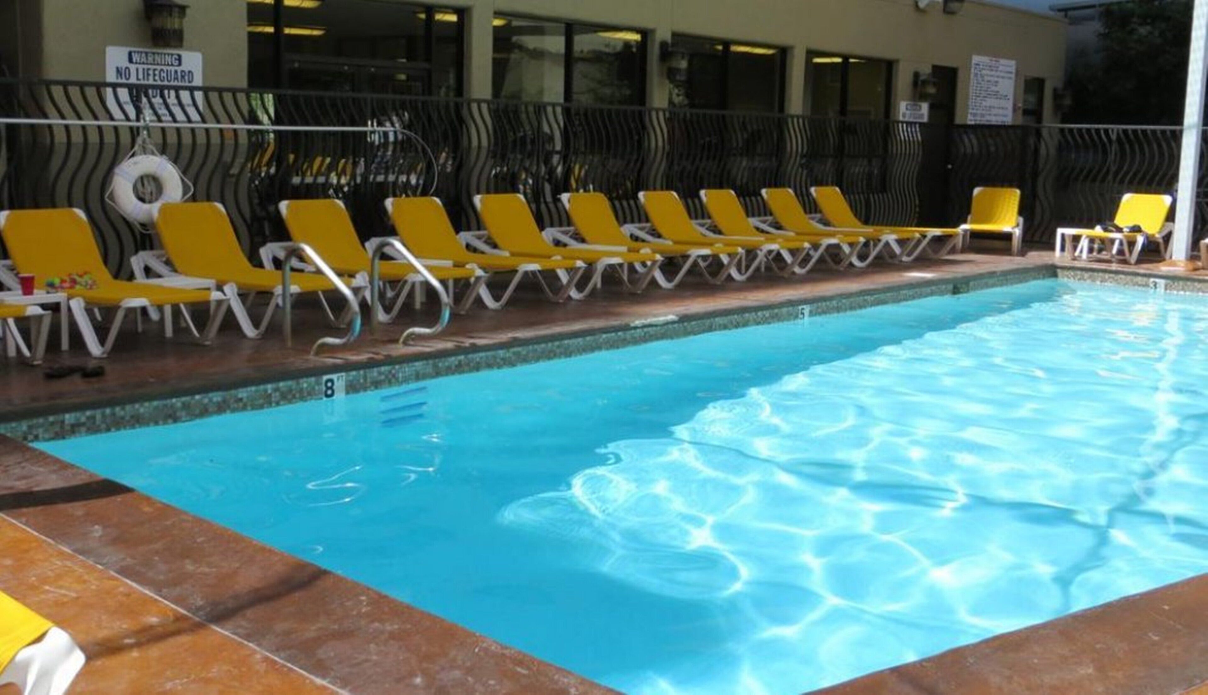 A swimming pool with yellow lounge chairs and a lifeguard warning sign.