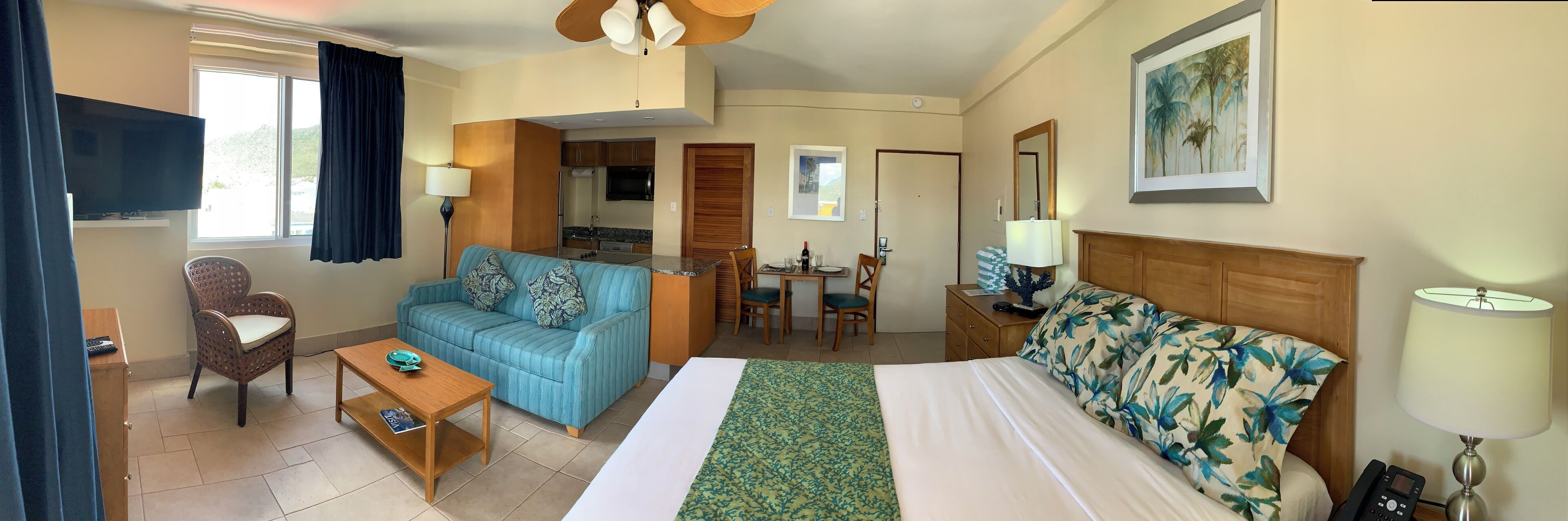 A hotel room with a bed, a sofa, a desk, a chair, a TV, and a dining area.