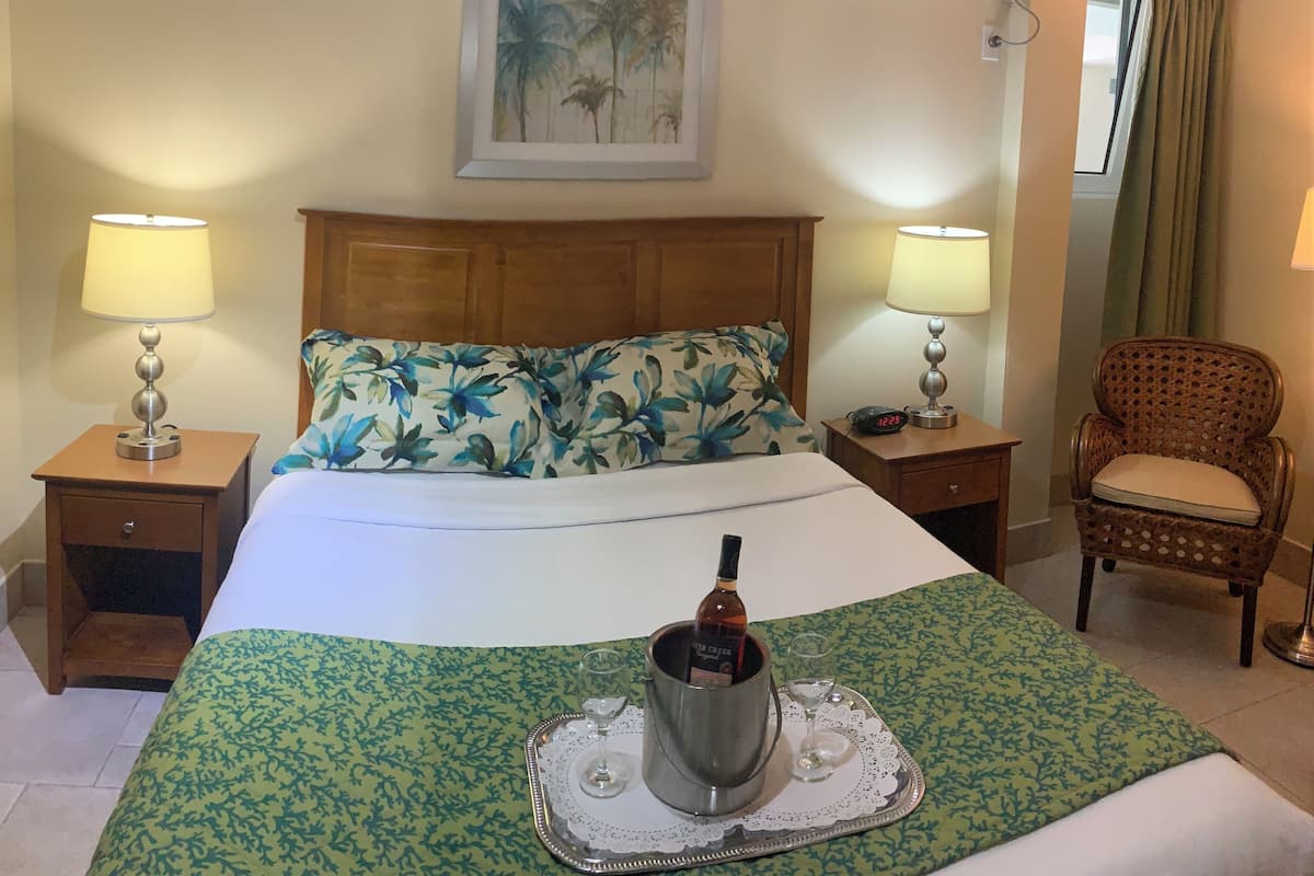Ein Hotelzimmer mit einem Bett, zwei Nachttischen mit Lampen, einem Sessel und einem Gemälde an der Wand sowie einer Klimaanlage.