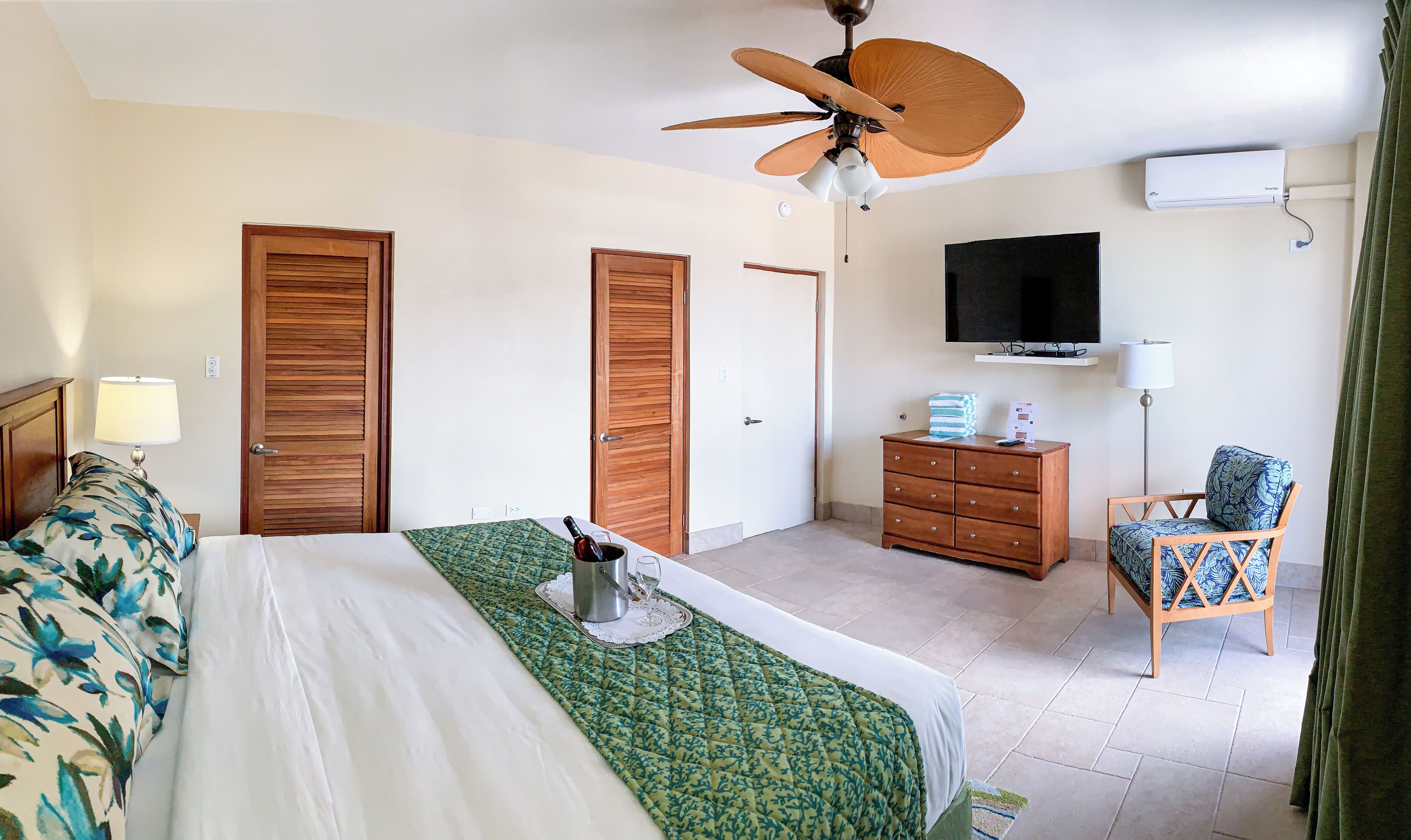 A hotel room with a bed, a wooden dresser, a television, and a ceiling fan.