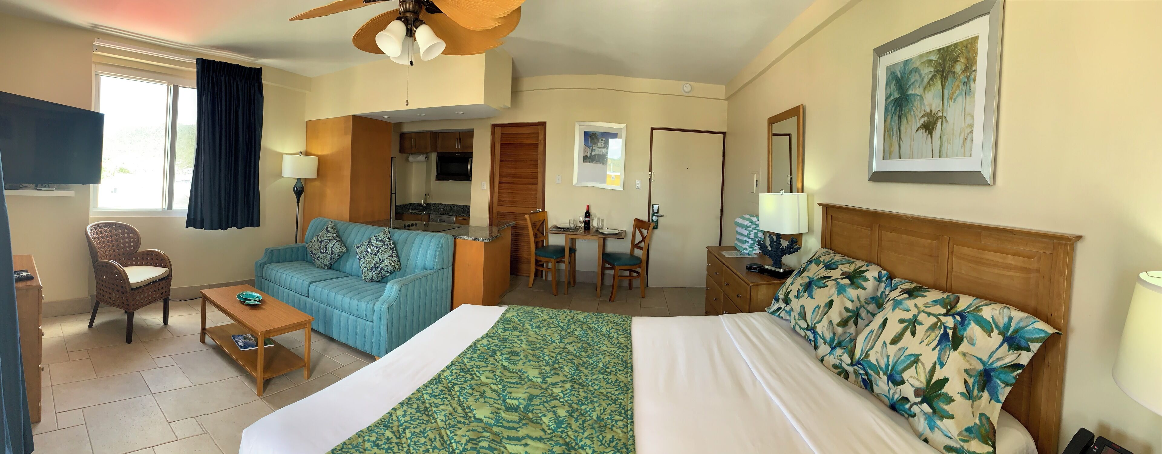 Quarto de hotel com cama, sofá, mesa de jantar com cadeiras, televisão e ventoinha no teto.