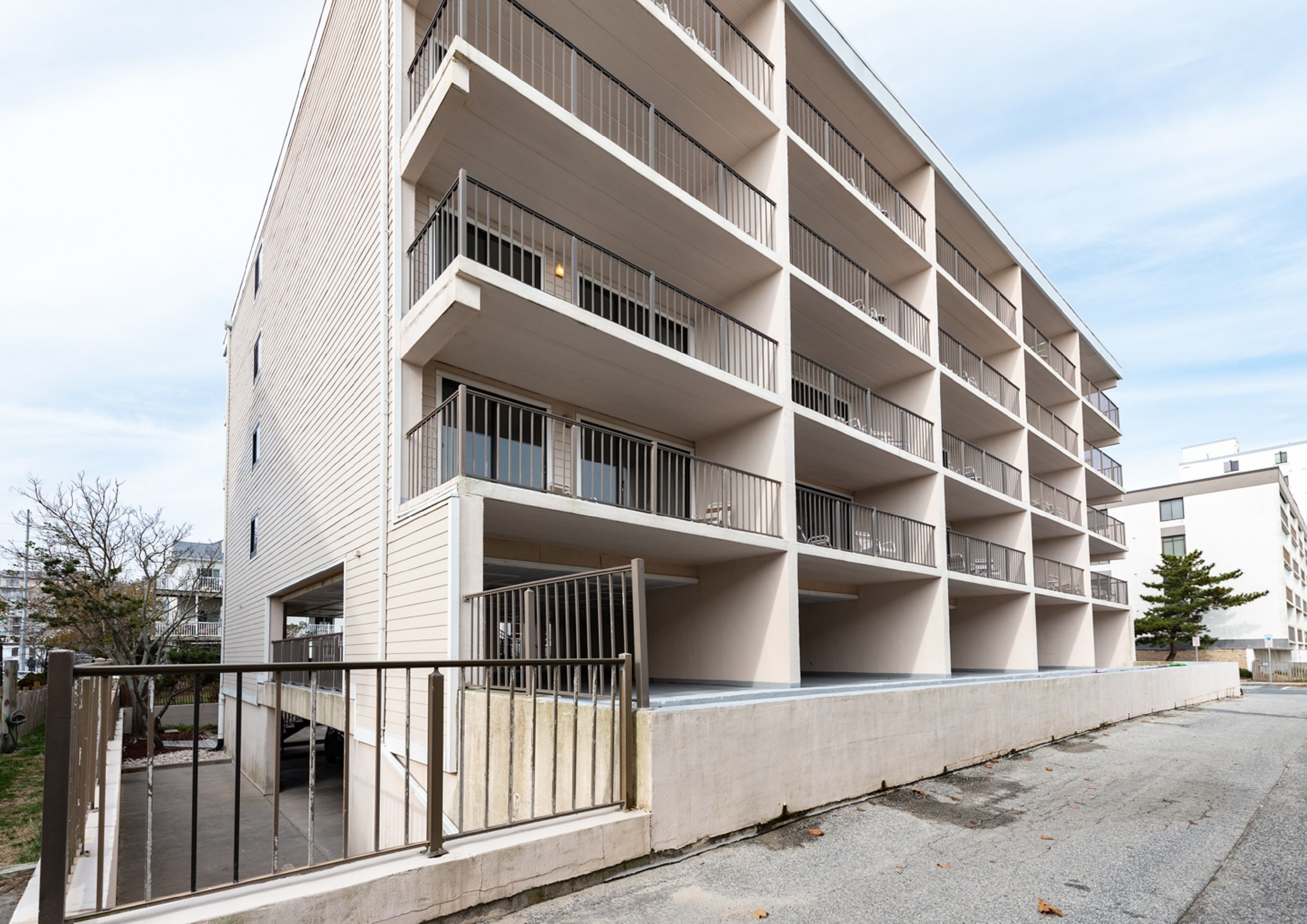 Un edificio de varios pisos con balcones, entrada porticada y un camino de hormigón.