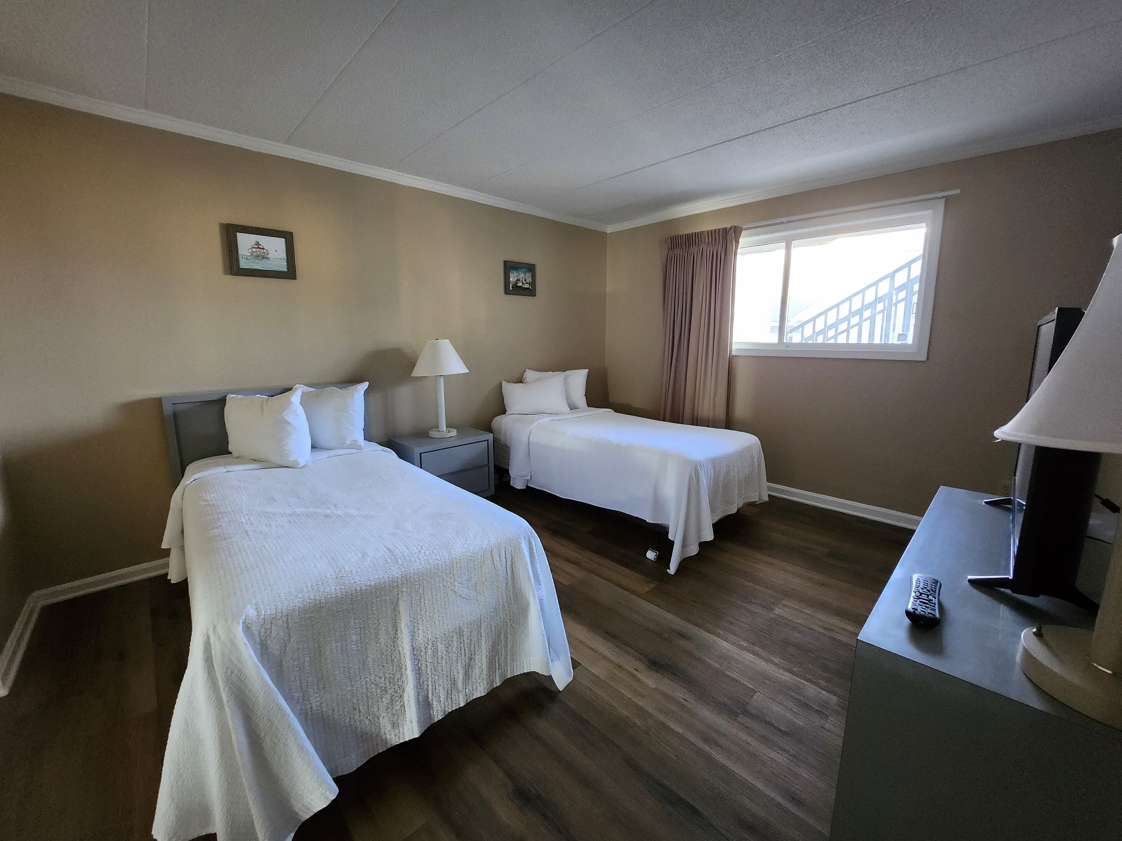 A hotel room with two beds, a desk, a lamp, and a window with curtains.