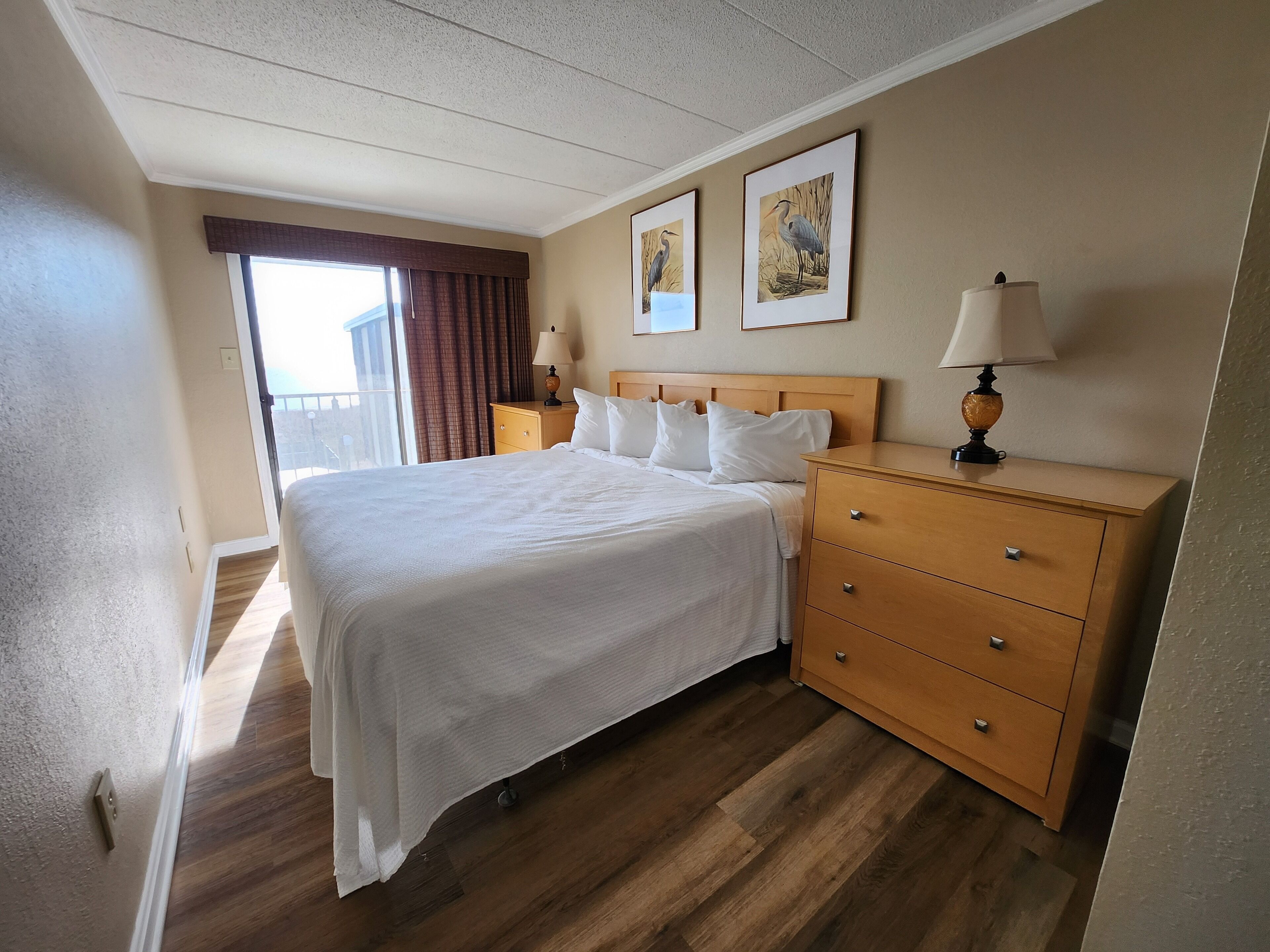 Ein Hotelzimmer mit einem großen Bett, einer Holzkommode, zwei Nachttischlampen und zwei gerahmten Bildern an der Wand.