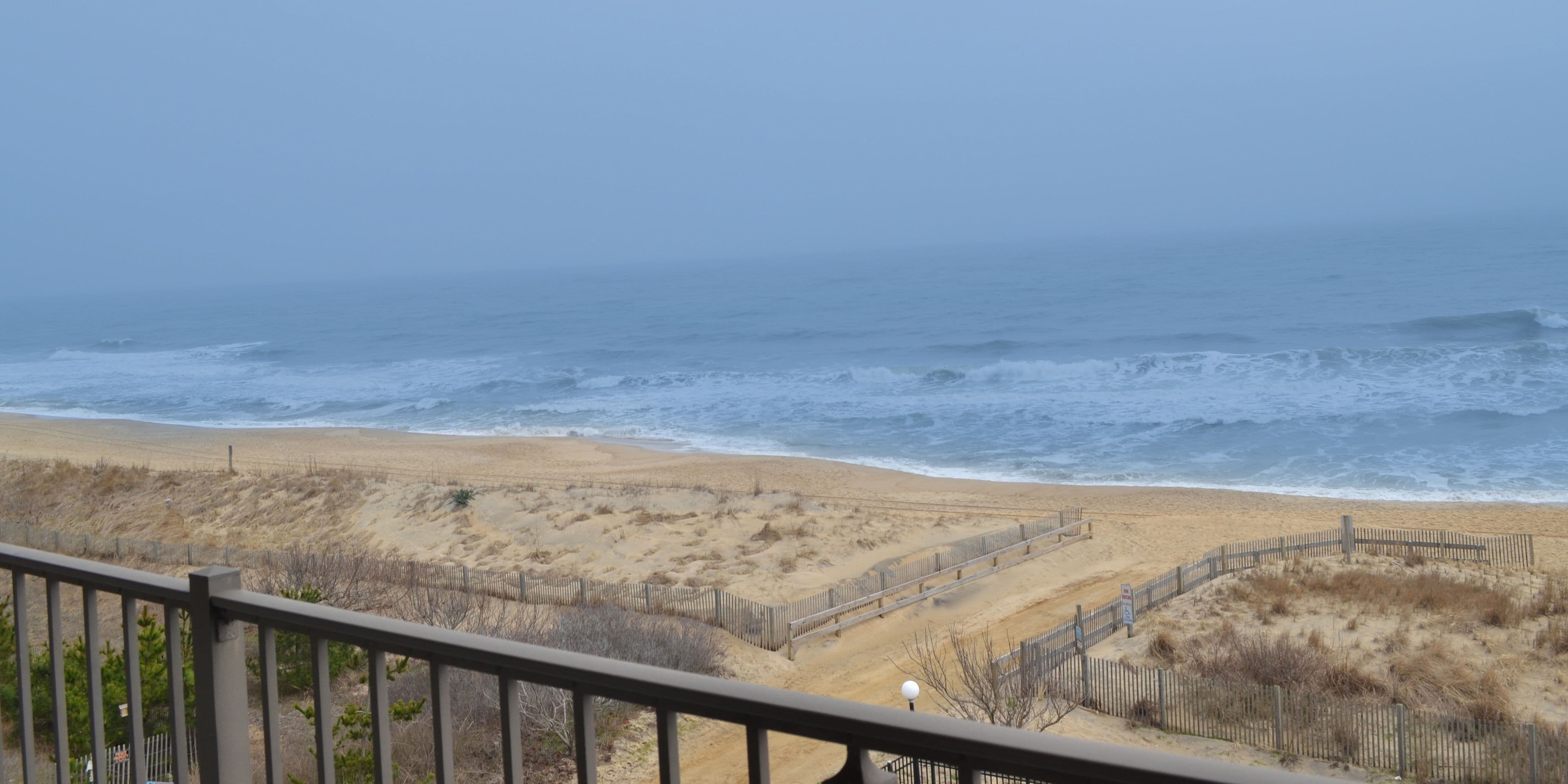 Une vue sur la plage, avec une clôture en bois et un sentier menant à l’océan.