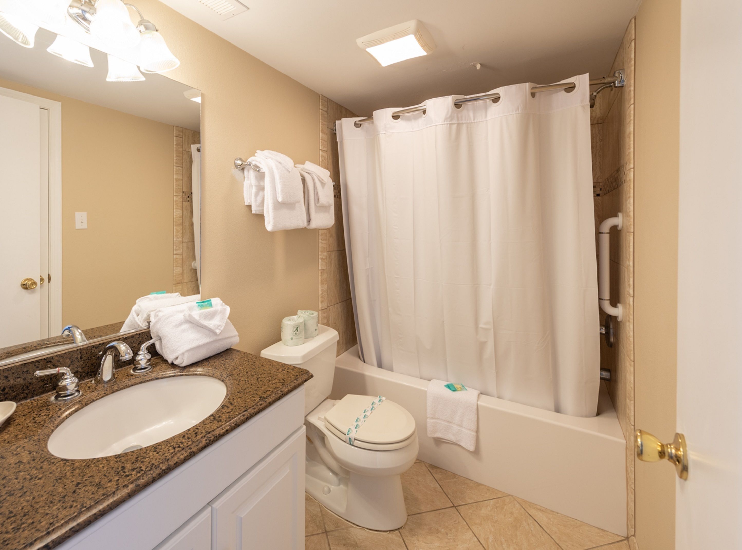 A bathroom with a sink, toilet, and bathtub. There are towels hanging on the wall and a shower curtain.