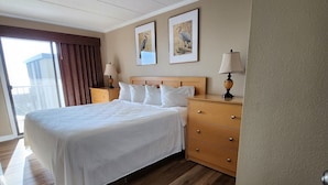Een hotelkamer met een groot bed, houten vloer, twee nachtkastjes met lampen en twee ingelijste foto's aan de muur.