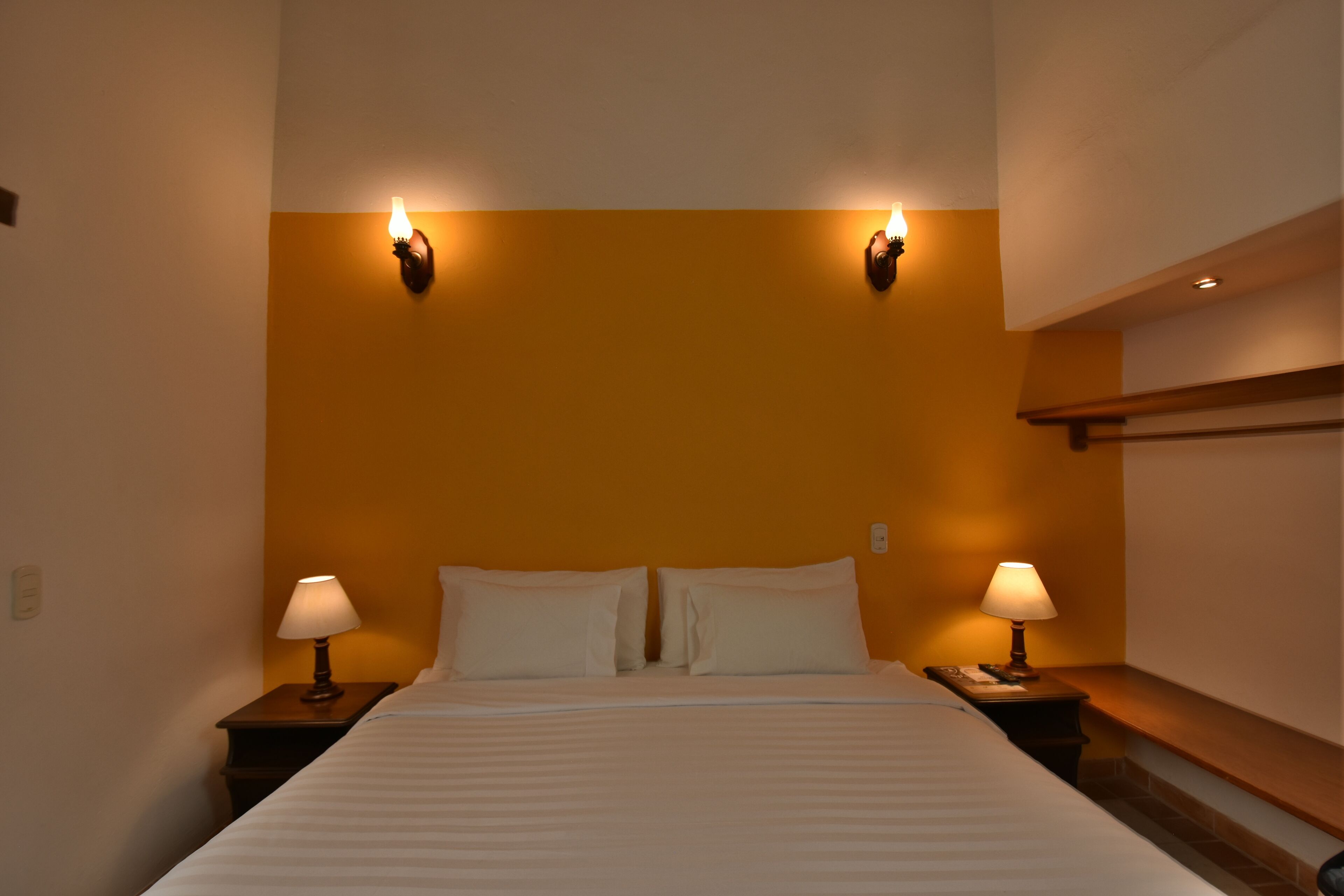 Een hotelkamer met een bed, twee bedlampjes en wandlampen.