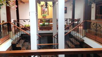 Un interior de varios niveles con una escalera central, barandillas de madera y plantas en macetas.