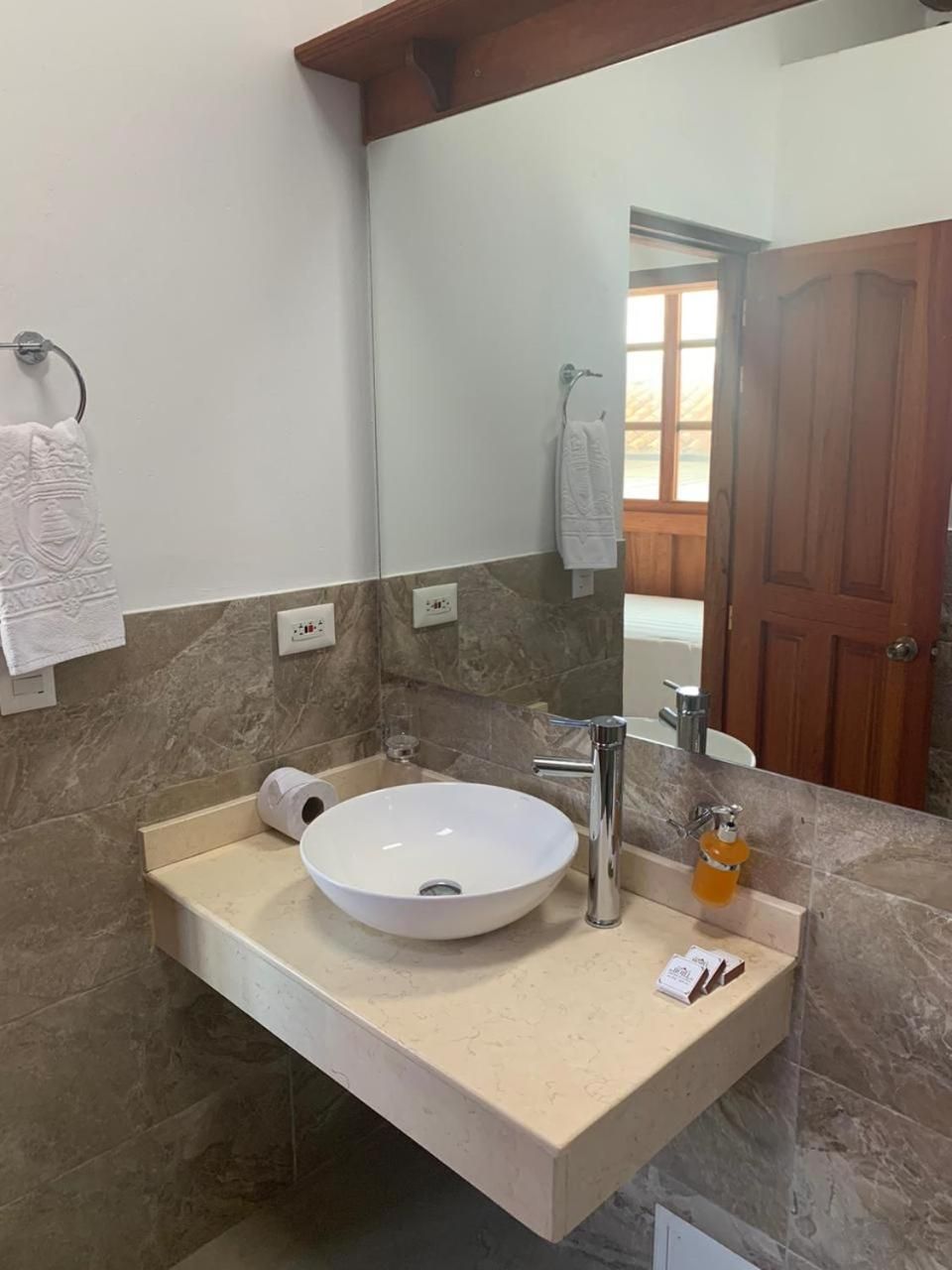 A bathroom with a large mirror, a white sink, and a wooden door.