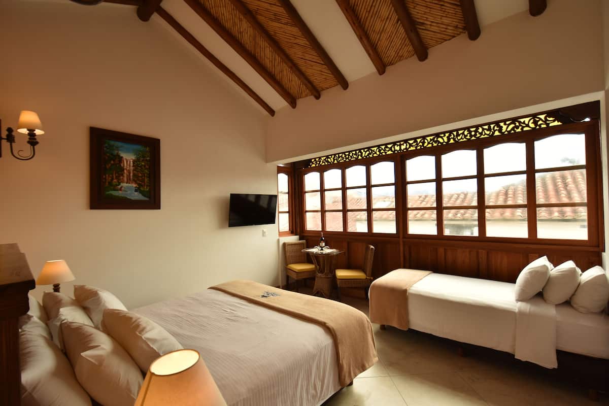 Ein Hotelzimmer mit Bett, Sofa, Fernseher, einem Fenster mit Blick auf Gebäude und einem Bild an der Wand.