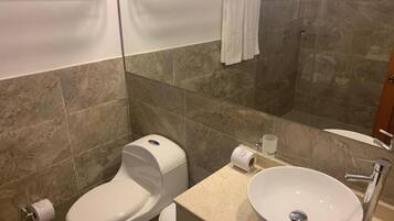 Un baño con inodoro, bidé, lavabo y cabina de ducha de vidrio.