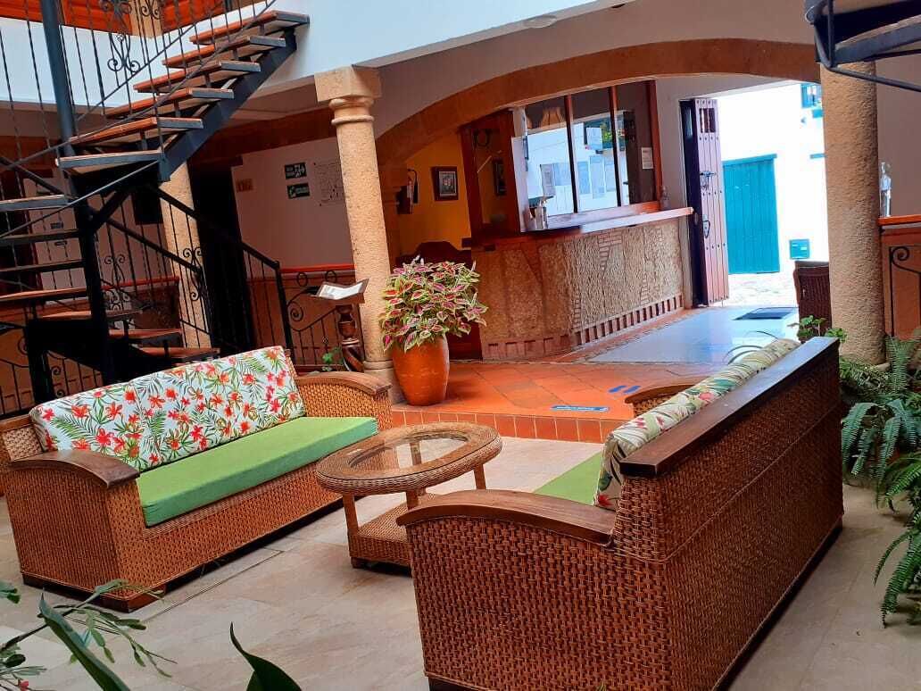 A lobby with a staircase, wicker furniture, a large potted plant, and a reception desk.