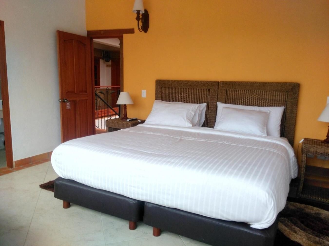 A spacious bedroom with a large bed, a wooden door, and a small table with a lamp.
