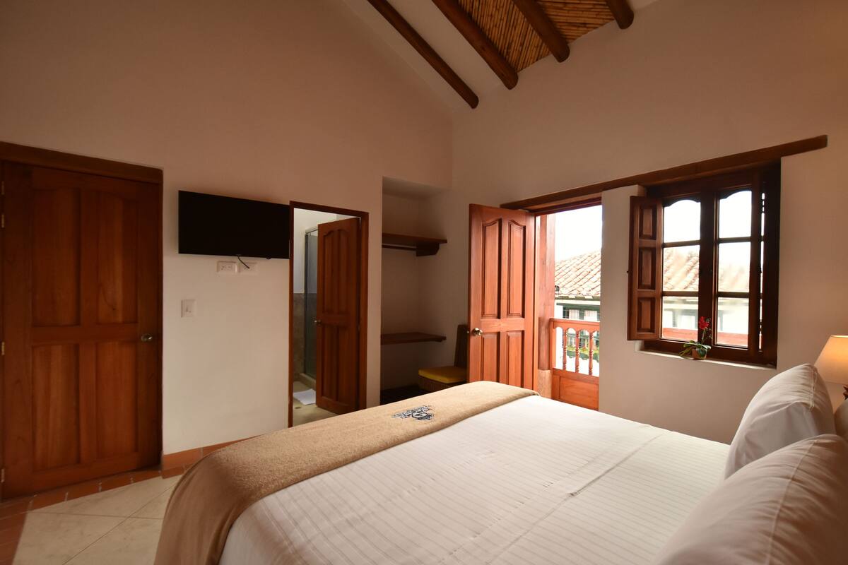 Ein Schlafzimmer mit Bett, Holztüren, einem an der Wand montierten Fernseher und einem Fenster mit Blick nach draußen.
