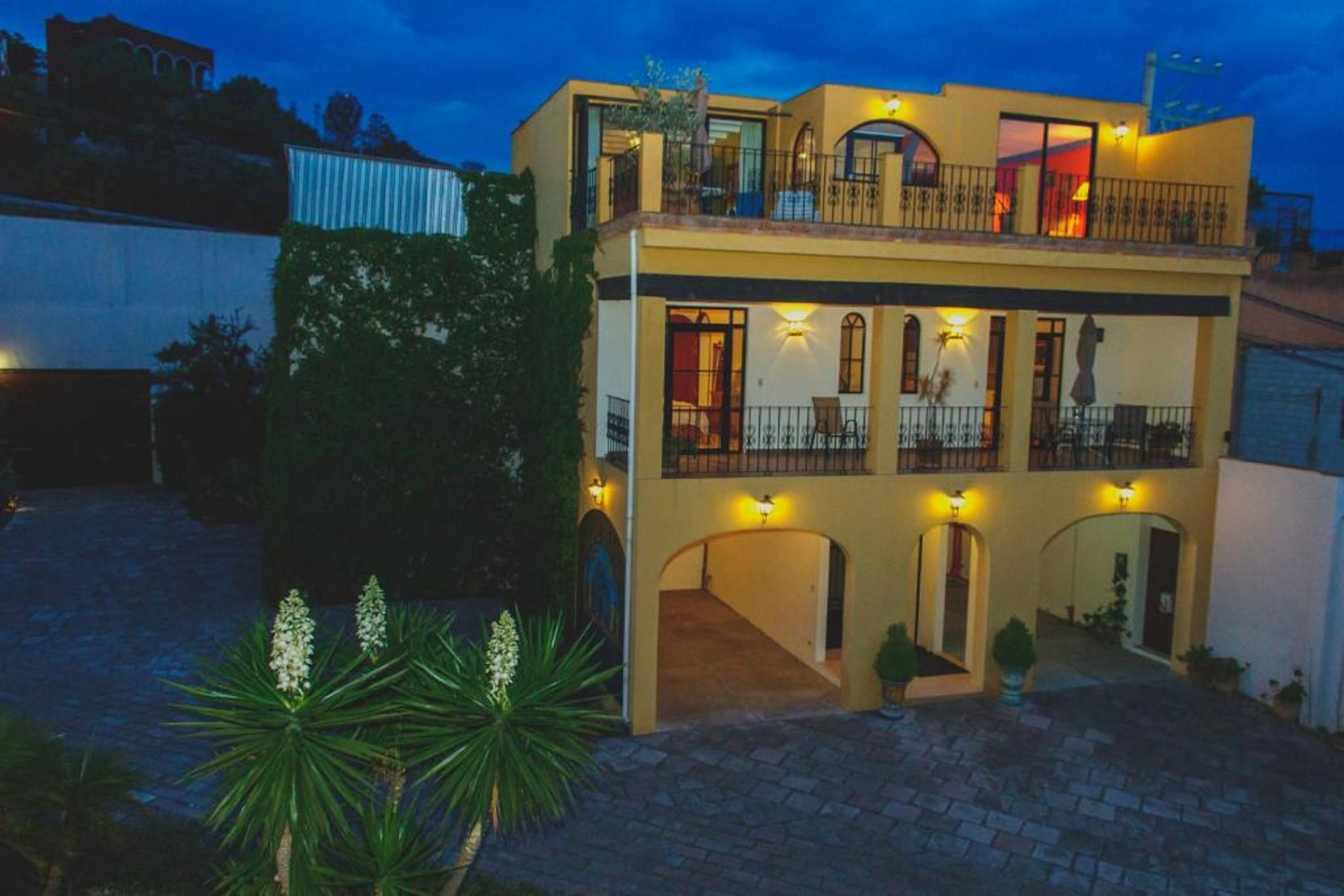 A two-story building with a balcony on the upper floor, a covered entrance, and a paved courtyard.