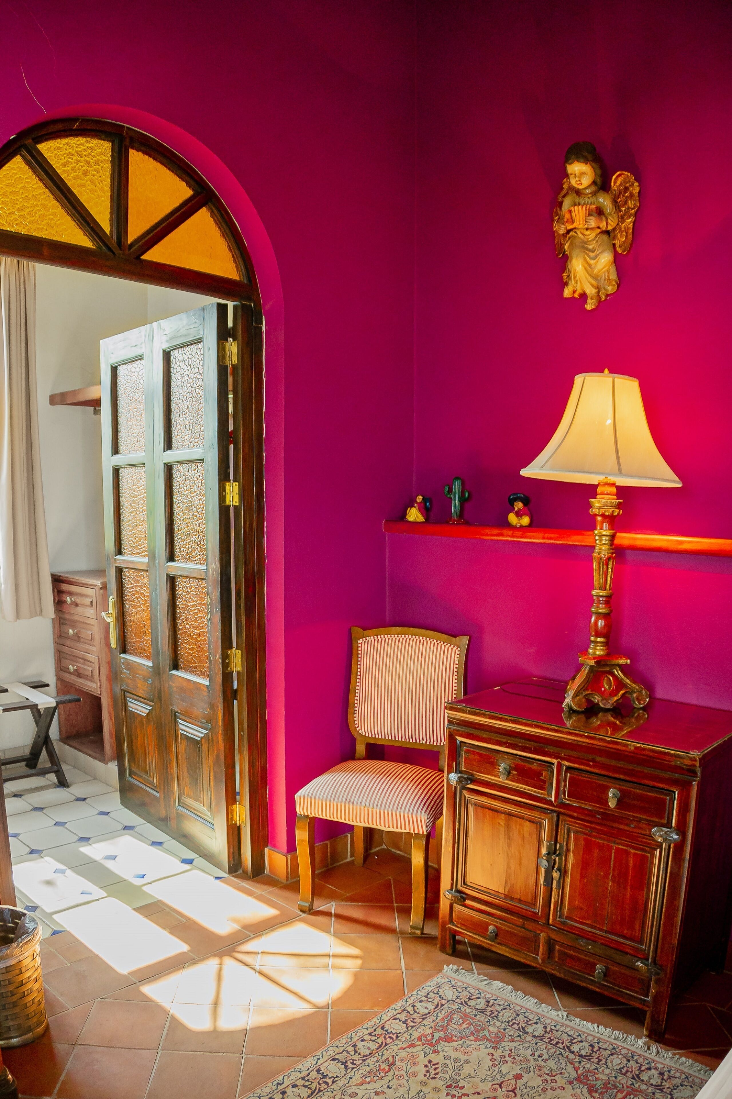 Une pièce avec un meuble en bois, une chaise, une lampe et une statuette d’ange décorative accrochée au mur.