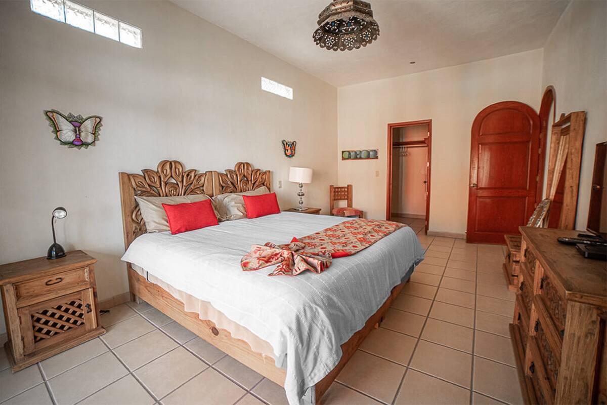 A bedroom with a large bed, wooden headboard, a nightstand, a dresser, and a door.
