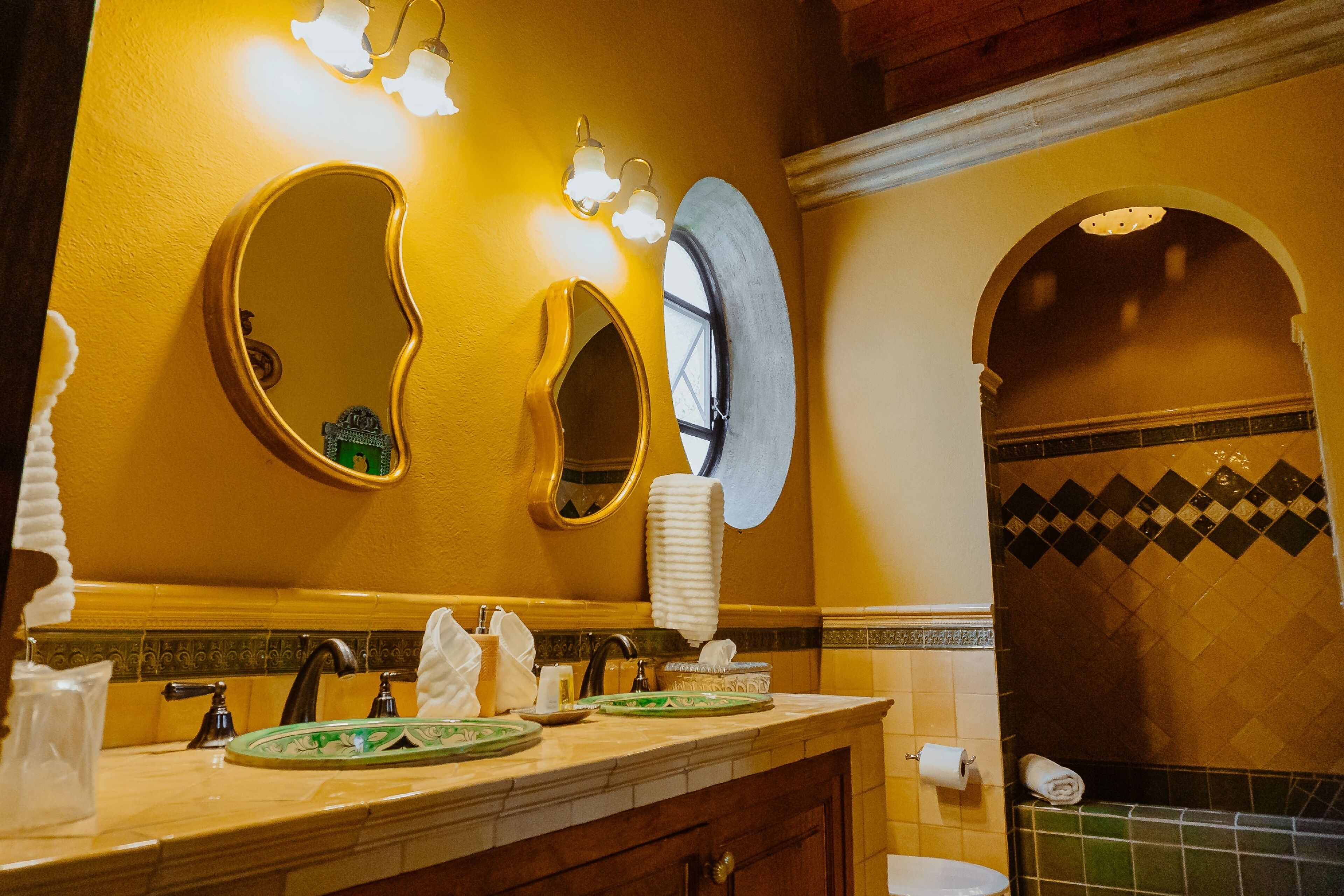 A bathroom with a vanity, two mirrors, a sink, and a window.