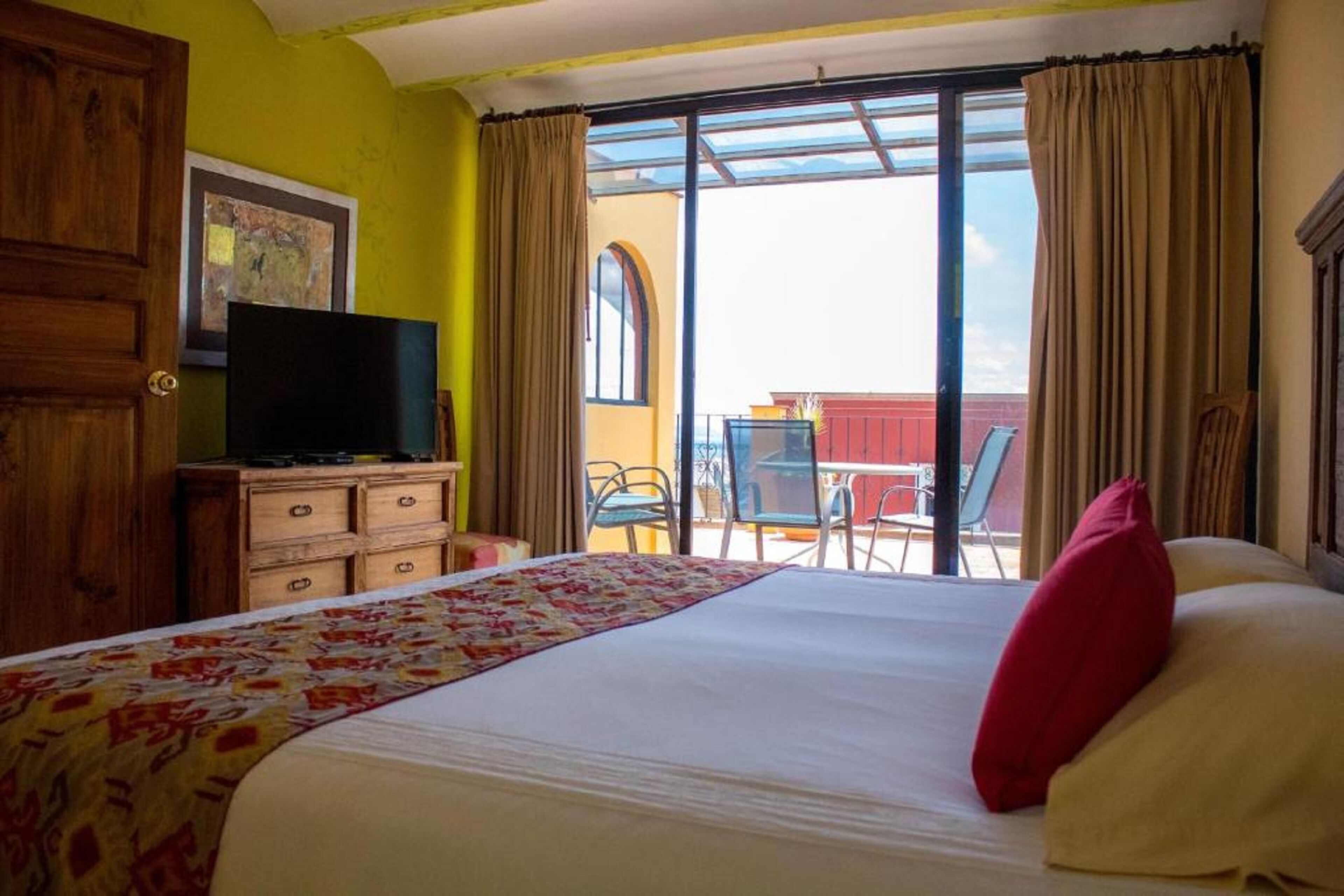 A hotel room with a bed, a television on a dresser, a balcony with chairs, and a table.