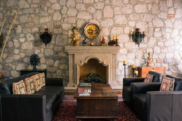 A stone-walled room with a fireplace, leather sofas, and a coffee table. - Casa Don Pascual Hotel Boutique Sweet Home (San Miguel de Allende)
