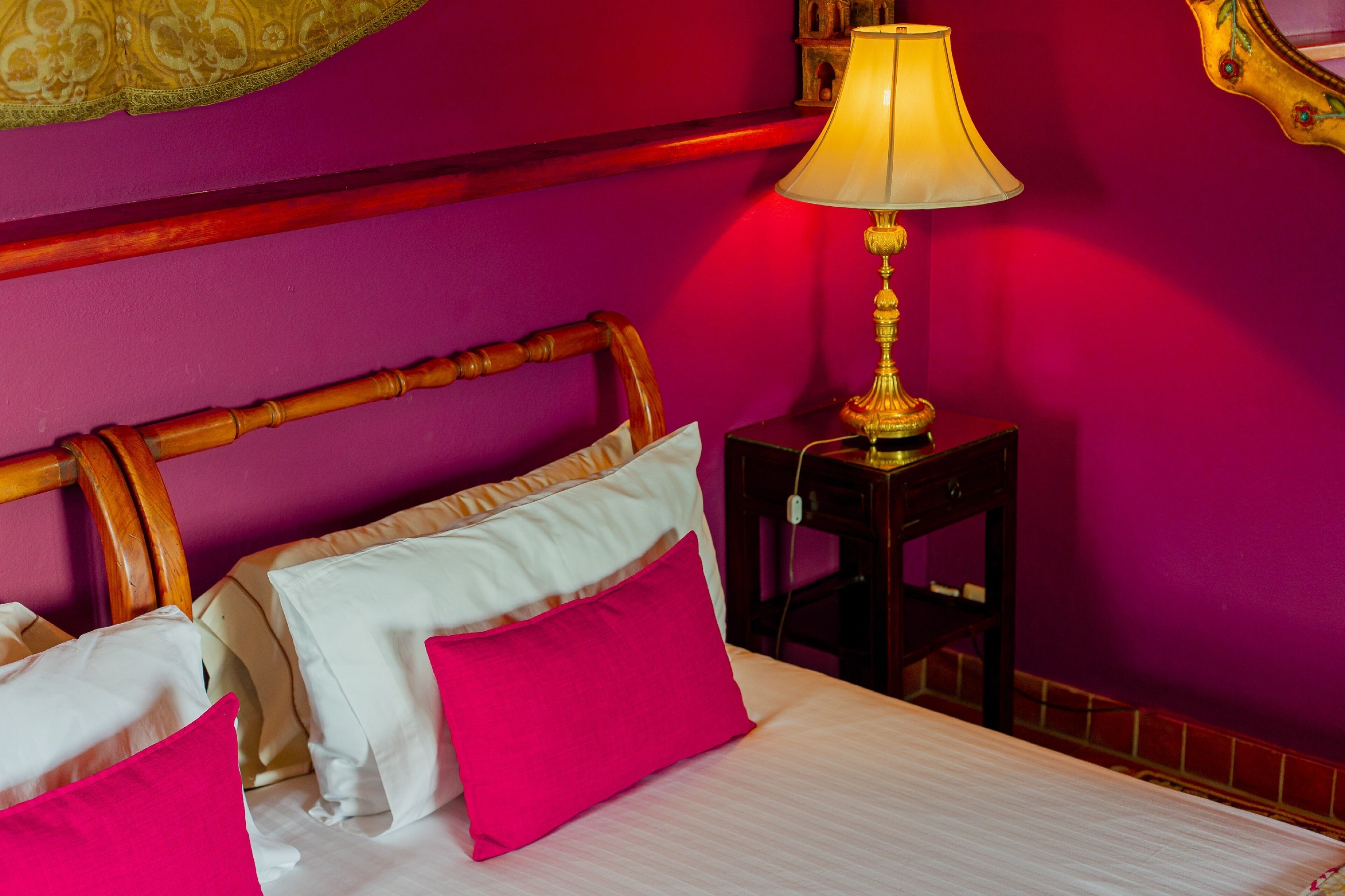 A bed with white and pink pillows, a wooden headboard, and a nightstand with a lamp.