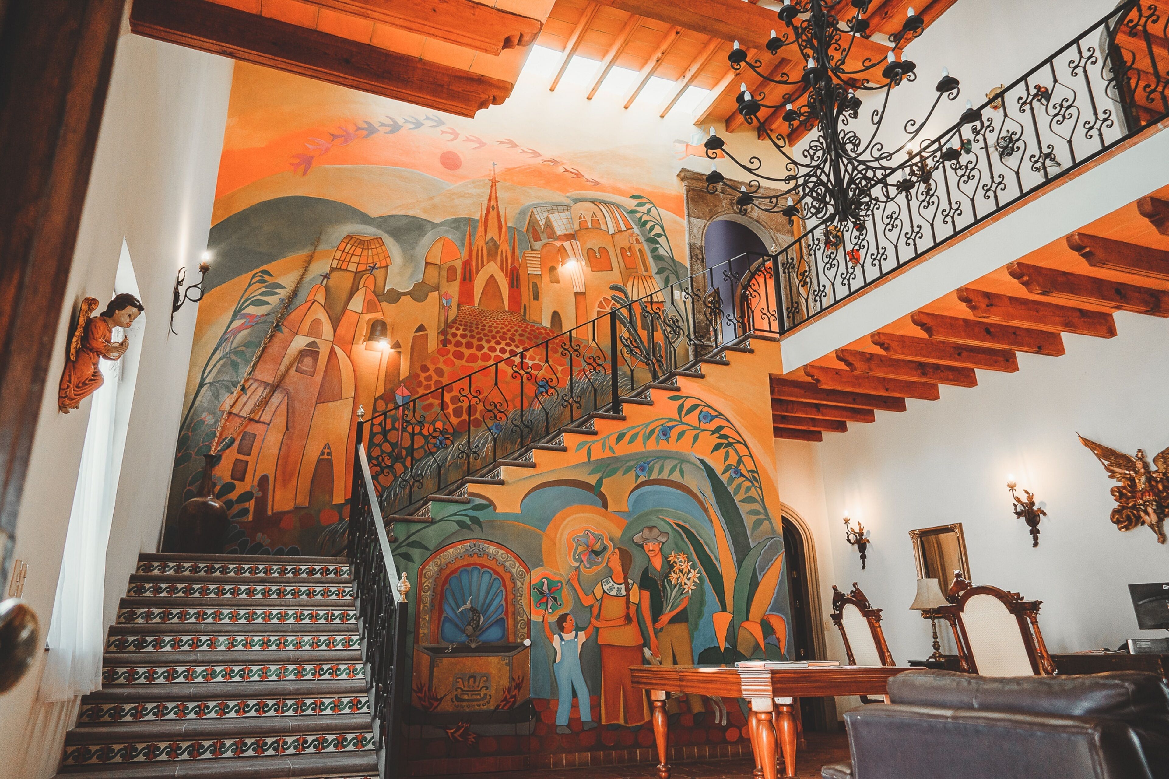 A staircase with a mural, wooden beams, and wrought iron railings.